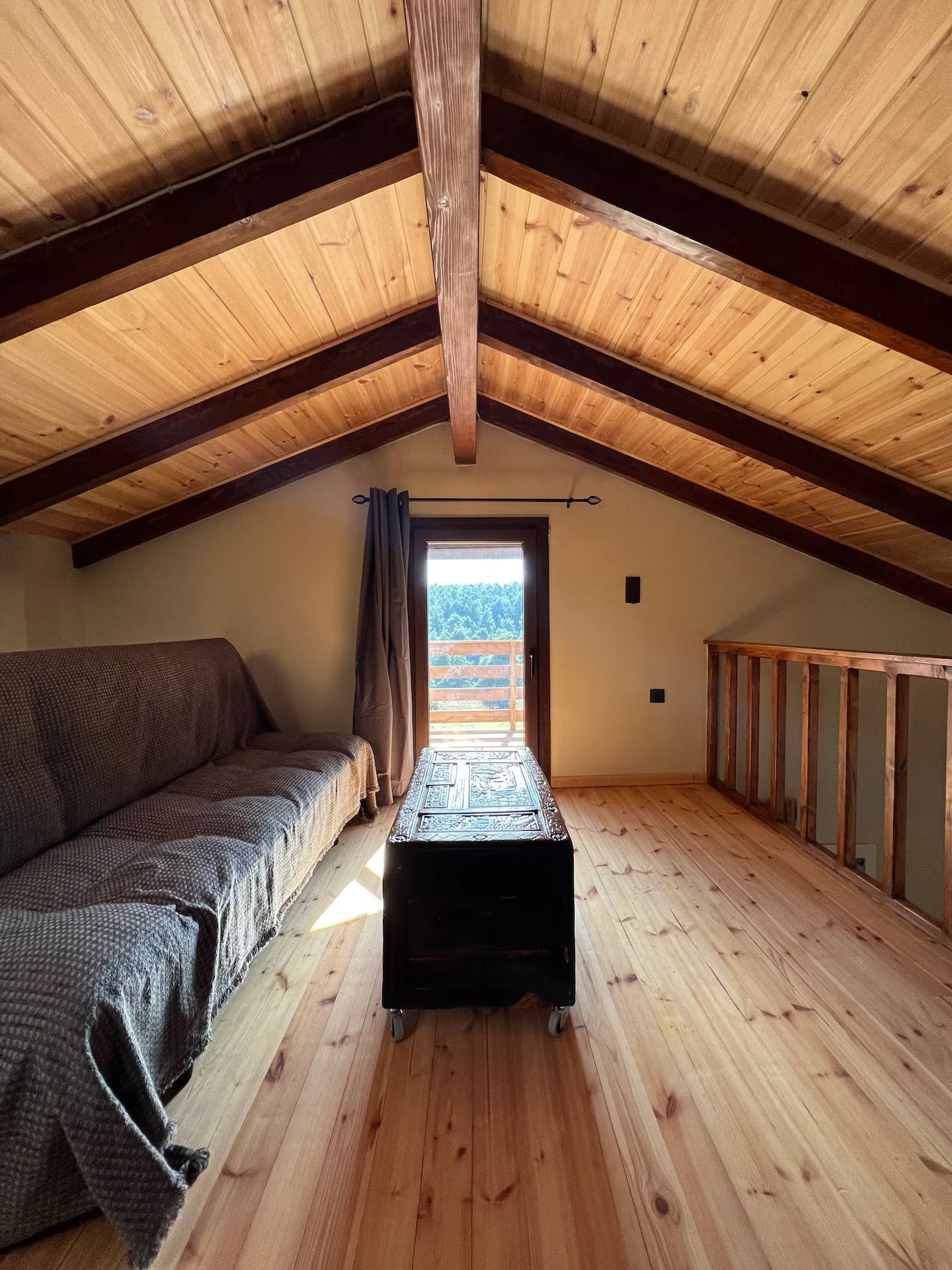 The attic under its pine ceiling, with the sofa bed and the door to the balcony