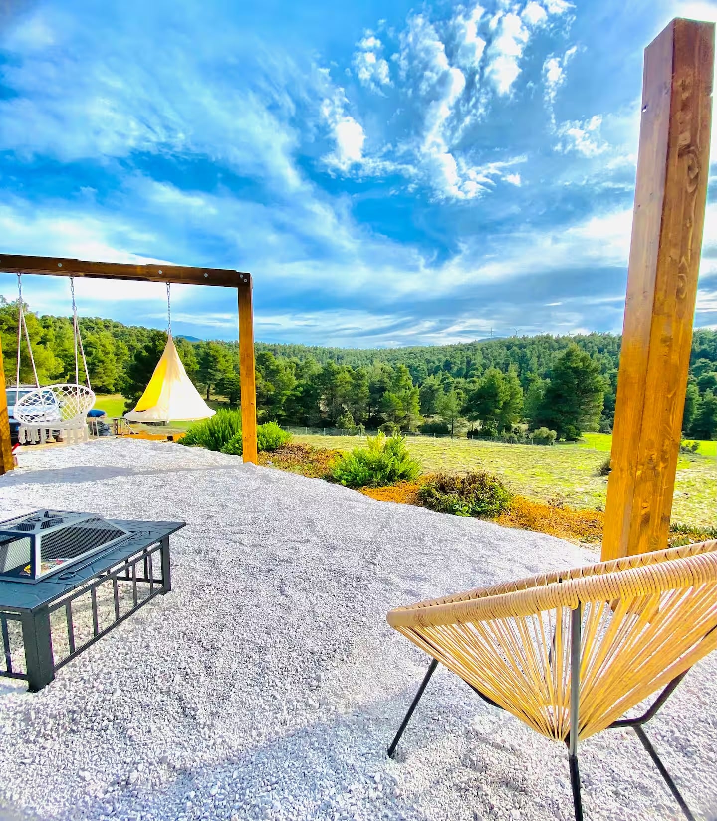The white-gravel terrace with the fire pit, a swing and a hanging tent, facing the forest