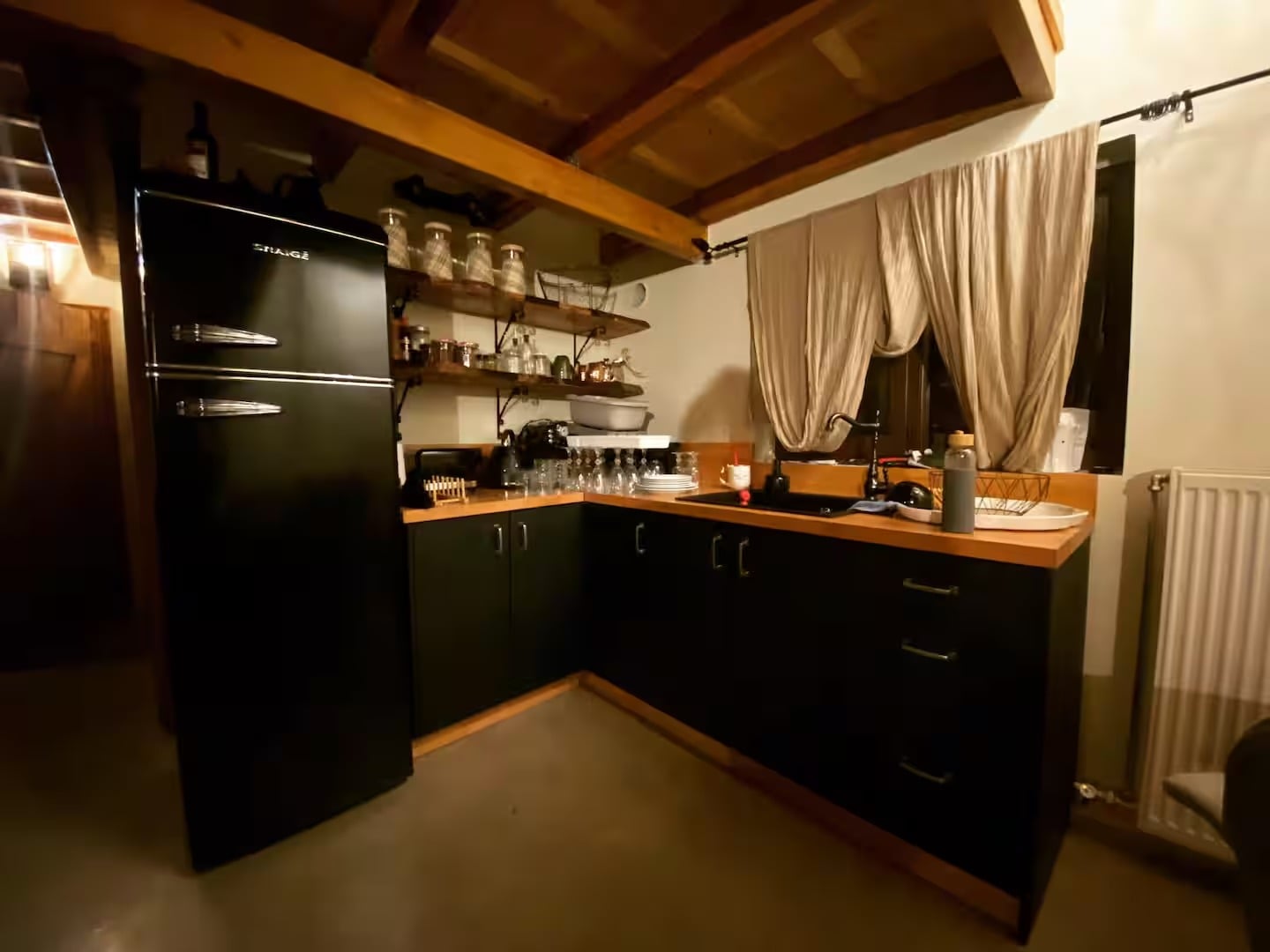 The indoor kitchen, with black cabinets, a wooden worktop and a retro black fridge