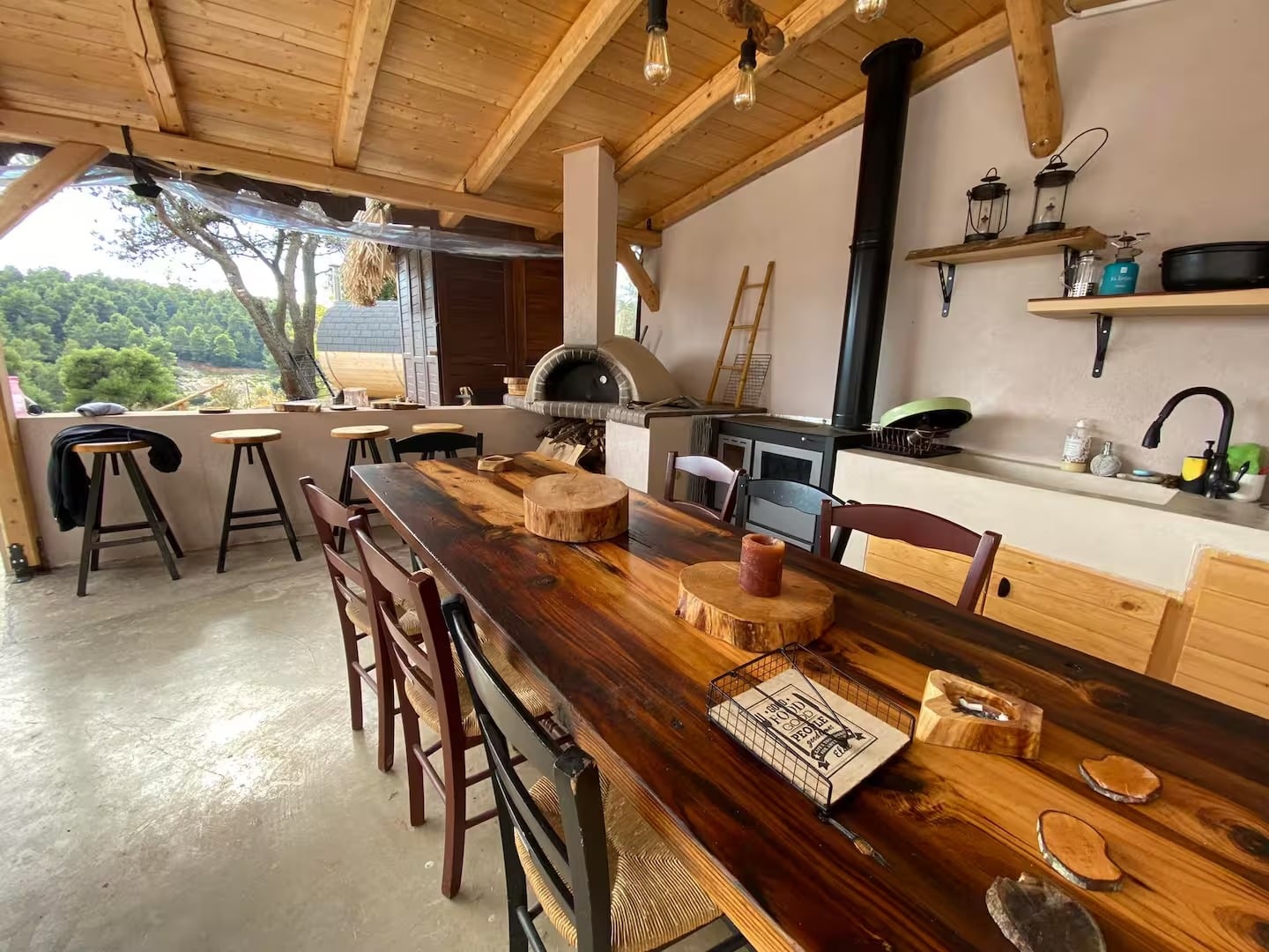 The outdoor kitchen with its long wooden table, wood oven and wood stove under a timber roof