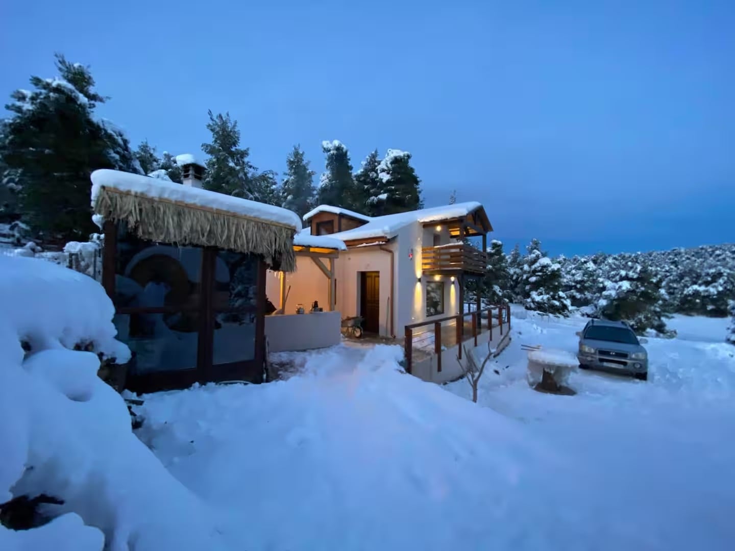 The house lit up at dusk in deep snow, with snow-covered pines behind it