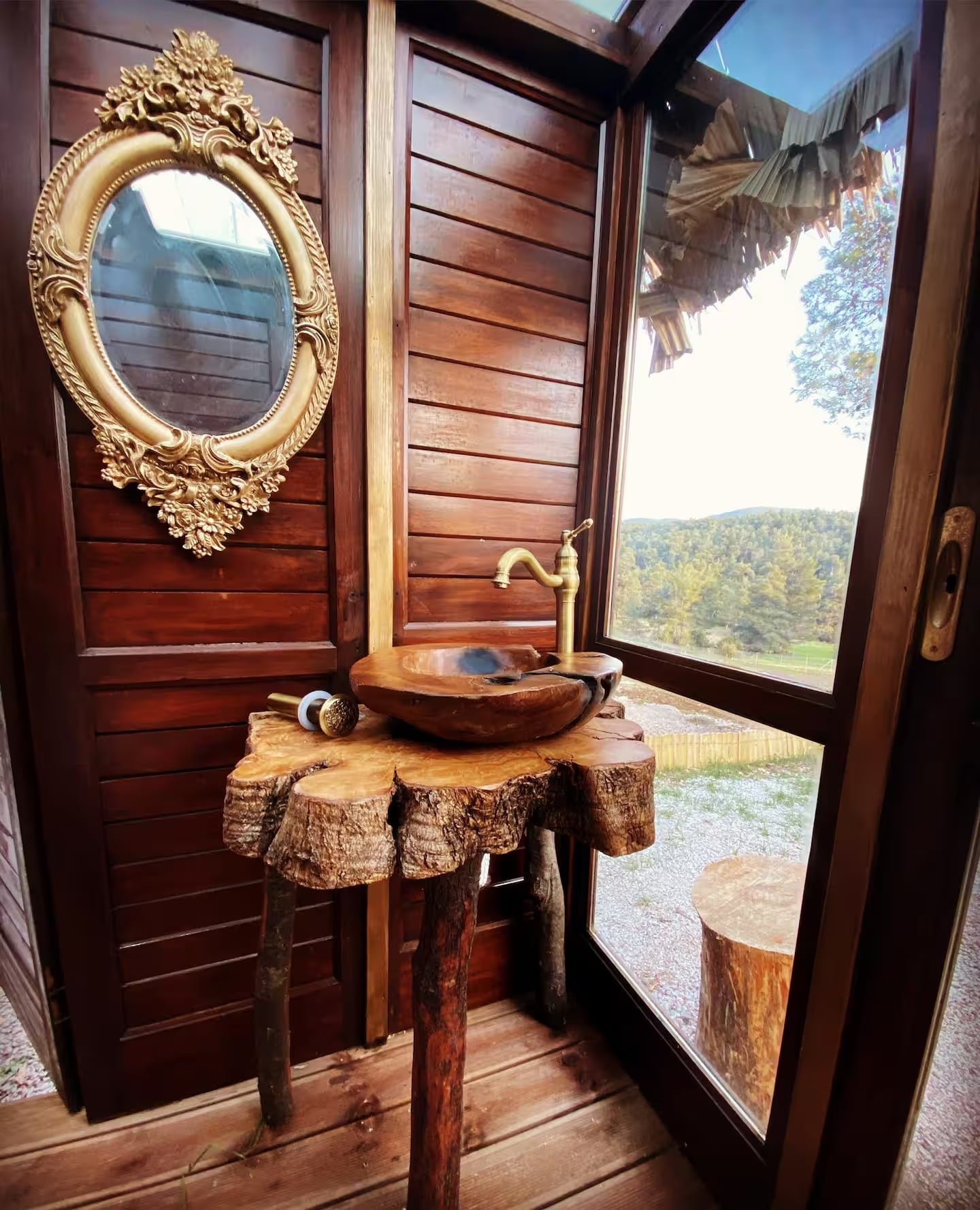 A wooden basin with a brass tap and a gilded mirror, looking out to the forest